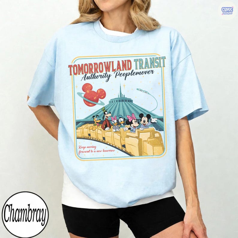 Puede incluir: Camiseta azul claro con un dise&ntilde;o de Tomorrowland Transit Authority Peoplemover. El gr&aacute;fico incluye a Mickey Mouse, Minnie Mouse, Goofy, Donald Duck y otros personajes en un tren, con el texto "Keep moving forward to a new tomorrow."