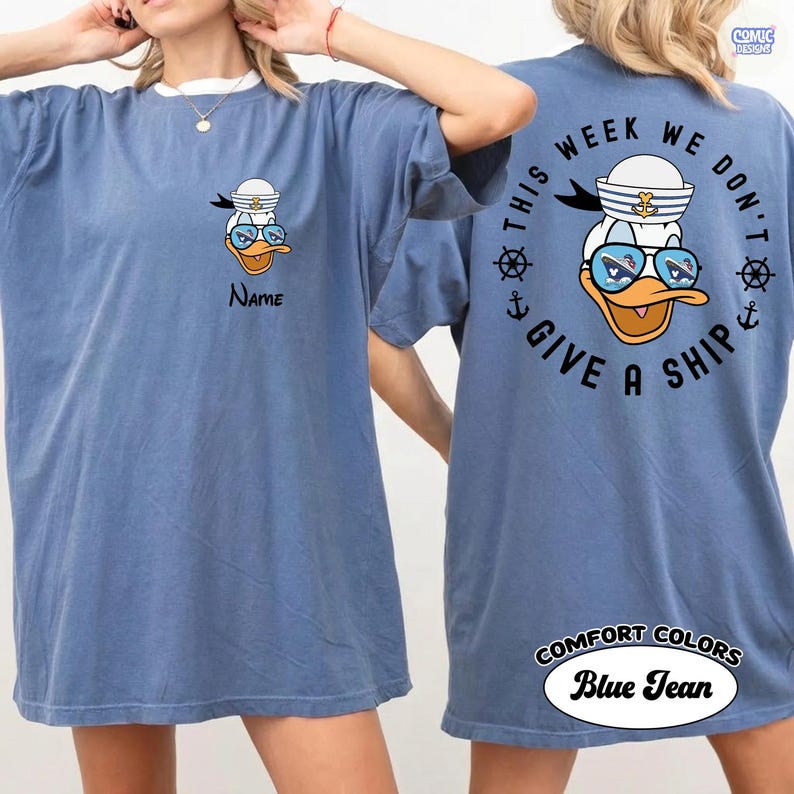 May include: Blue jean-colored t-shirt with a cartoon duck wearing a sailor hat and sunglasses. The front of the shirt has the word "Name" below the duck. The back of the shirt says "This week we don't give a ship."