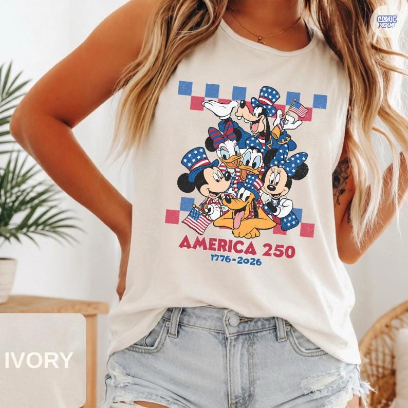 May include: An ivory sleeveless tank top featuring a graphic print of Mickey Mouse, Minnie Mouse, Donald Duck, Daisy Duck, Goofy, and Pluto wearing patriotic hats. The text reads AMERICA 250 1776-2026, set against a red and blue checkered background.