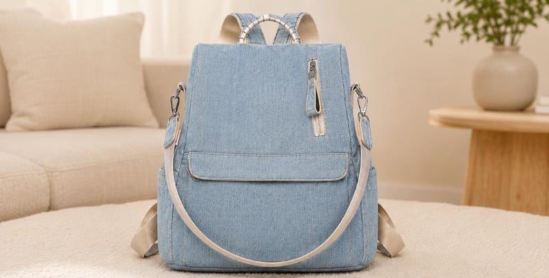 Puede incluir: Una mochila de mezclilla azul claro con un bolsillo vertical con cremallera en la parte delantera, un bolsillo horizontal con solapa y correas beige para los hombros. La bolsa incluye herrajes de metal plateado, un asa superior y bolsillos laterales.