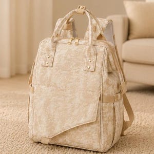 Peut inclure: Un sac &agrave; dos au motif marbr&eacute; beige et cr&egrave;me dot&eacute; d'un compartiment principal rectangulaire, d'une poche avant avec rabat diagonal, de deux poign&eacute;es sup&eacute;rieures, de fermetures &eacute;clair dor&eacute;es et de bretelles r&eacute;glables avec rembourrage en maille.