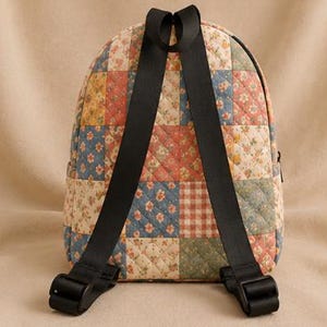K&ouml;nnte beinhalten: Ein gesteppter Rucksack mit einem Patchwork-Design aus verschiedenen Blumen- und Karomustern in gedeckten Blau-, Rot-, Gelb- und Cremet&ouml;nen. Die Tasche verf&uuml;gt &uuml;ber zwei schwarze, verstellbare Schultergurte und einen Tragegriff an der Oberseite.