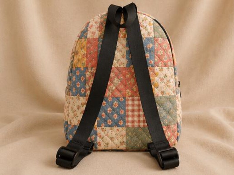K&ouml;nnte beinhalten: Ein gesteppter Rucksack mit einem Patchwork-Design aus verschiedenen Blumen- und Karomustern in gedeckten Blau-, Rot-, Gelb- und Cremet&ouml;nen. Die Tasche verf&uuml;gt &uuml;ber zwei schwarze, verstellbare Schultergurte und einen Tragegriff an der Oberseite.