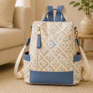 May include: A backpack featuring a beige and white geometric diamond pattern with blue trim. It includes a vertical zippered front pocket with a gold-toned pull, two side pockets, and adjustable light-colored shoulder straps with blue accents.
