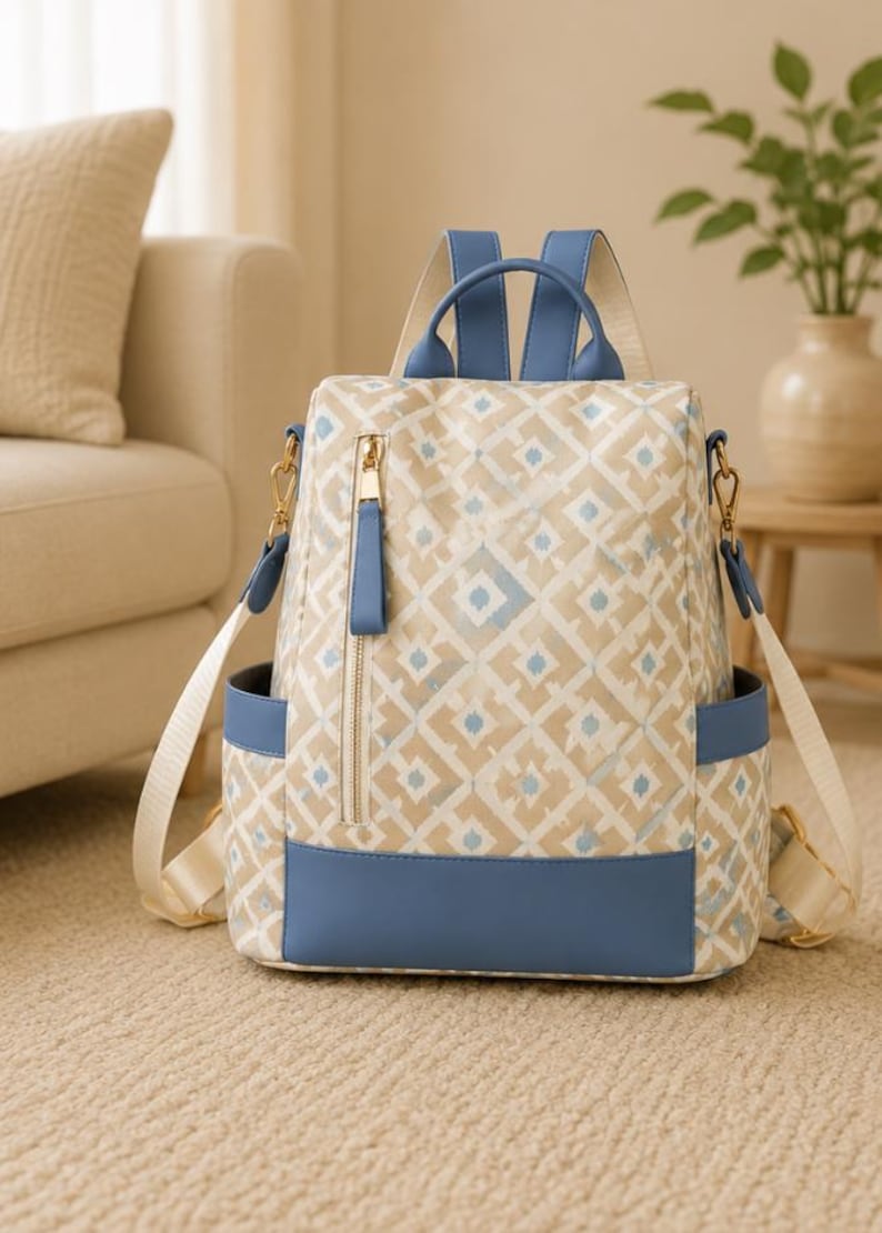 May include: A backpack featuring a beige and white geometric diamond pattern with blue trim. It includes a vertical zippered front pocket with a gold-toned pull, two side pockets, and adjustable light-colored shoulder straps with blue accents.