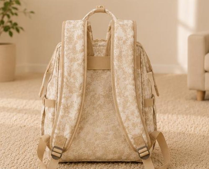Peut inclure: Un sac &agrave; dos beige et cr&egrave;me arborant un motif floral d&eacute;licat sur toute sa surface ext&eacute;rieure. Le sac comprend deux bretelles rembourr&eacute;es, une poign&eacute;e de transport sup&eacute;rieure et des sangles r&eacute;glables avec des boucles en m&eacute;tal.