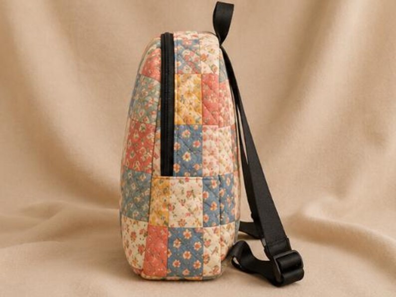 K&ouml;nnte beinhalten: Ein gesteppter Rucksack mit einem Patchwork-Design aus Blumenmustern in Blau-, Gelb- und Korallent&ouml;nen. Die Tasche verf&uuml;gt &uuml;ber einen schwarzen Rei&szlig;verschluss an der Seite, einen schwarzen Tragegriff und verstellbare schwarze Nylongurte.