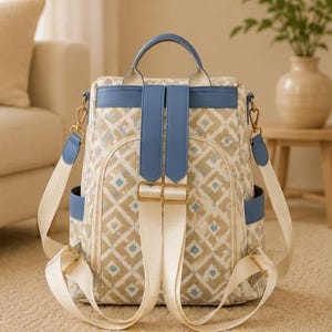 May include: A backpack featuring a beige and white diamond pattern with small blue accents. It includes blue leather-like trim, a top handle, adjustable cream-colored fabric shoulder straps, gold-tone metal hardware, and side pockets.