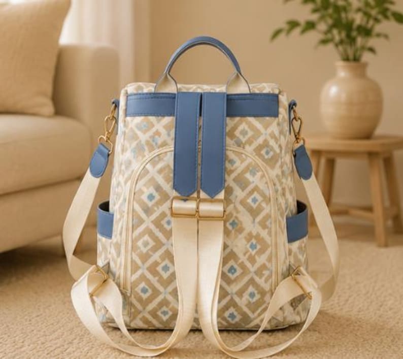 May include: A backpack featuring a beige and white diamond pattern with small blue accents. It includes blue leather-like trim, a top handle, adjustable cream-colored fabric shoulder straps, gold-tone metal hardware, and side pockets.