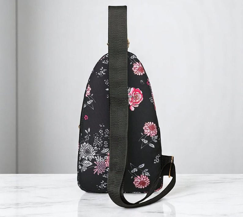 May include: A black floral print crossbody bag with a long adjustable strap. The bag has a small zippered pocket on the front and a flap closure.