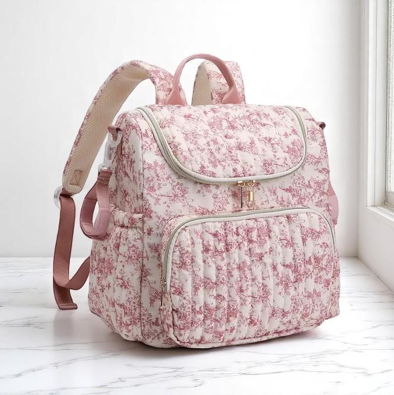 Puede incluir: Una mochila acolchada con un estampado floral en tonos rosa y blanco. La bolsa tiene un asa superior, correas ajustables para los hombros y m&uacute;ltiples compartimentos con cremallera. Los herrajes son dorados.