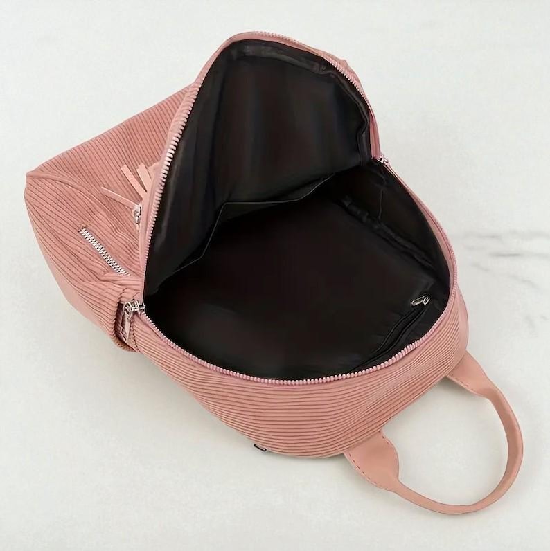 May include: A pink backpack with a textured, ribbed design. The bag has a top handle, a front zipper, and a tassel detail. The interior is black with multiple compartments. The backpack is open, revealing the inside.