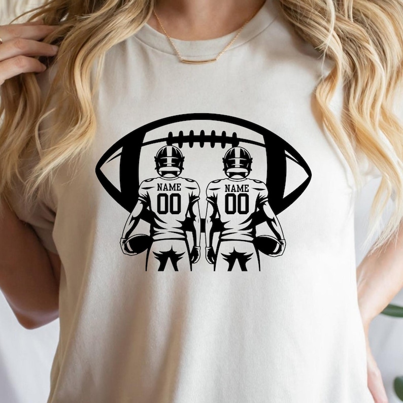 May include: A cream-colored t-shirt featuring a black graphic of two football players with the text "NAME" and the number "00" on their jerseys. A large black football shape is behind the players.
