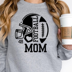 May include: A gray sweatshirt with a black football helmet and football graphic. The word "FOOTBALL" is printed vertically, with "MOM" below. A heart and the number "48" are also included in the design.