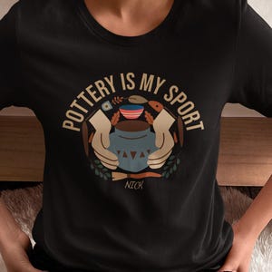 May include: Black t-shirt featuring the text "POTTERY IS MY SPORT" in a circular design. The design includes a pottery wheel, hands, and pottery. The name "NICK" is below the design.