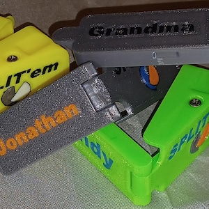 May include: Four colorful plastic containers with the words "SPLIT'em" and "Grandma" printed on them. The containers are stacked on top of each other and have a textured surface.