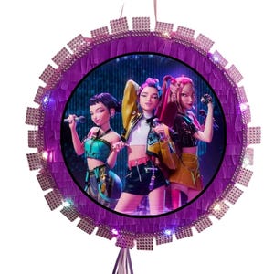 May include: A round, purple piñata featuring a vibrant image of three animated figures holding microphones. The piñata is trimmed with a textured border and small, square accents, and has a hanging ribbon.