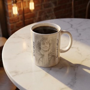 May include: A white ceramic coffee mug filled with dark coffee. The mug features a pencil sketch of a person and the phrases "What about" and "Second Coffee?" The mug is on a white marble table.