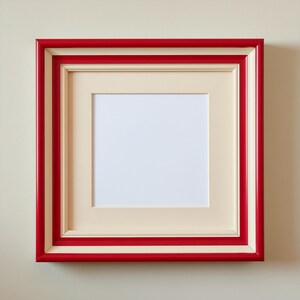 May include: Square picture frame with a red and cream border. The frame has a cream-coloured mount and a white interior space for a photo or artwork. Designed to be hung on a wall.