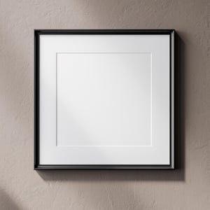May include: Square black picture frame with a white mat. The frame is mounted on a textured, neutral-toned wall. The frame is empty, ready for a photograph or artwork.