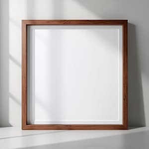 Może przedstawiać: Kwadratowa drewniana rama obrazu z ciemnobrązowym wykończeniem. Rama ma białe passe-partout i puste białe miejsce na zdjęcie lub grafikę. Rama stoi na białej powierzchni.