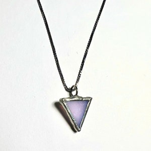 Op de afbeelding: Een zilveren ketting met een driehoekige hanger van helder glas met een lichtpaarse tint.