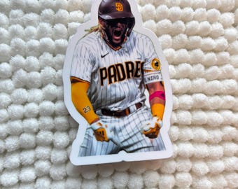 May include: A sticker featuring a baseball player in a Padres uniform. The player is wearing a brown helmet and a white and brown striped jersey with the word "Padres" across the chest. The player is in an action pose, with arms raised and mouth open.