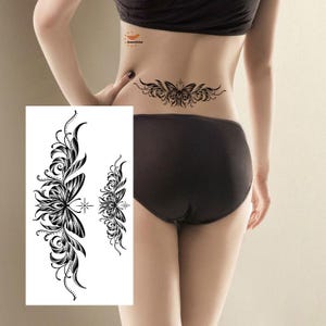 May include: Black and white temporary tattoos featuring floral and butterfly designs. The tattoos include a large vertical design and a smaller, symmetrical design. The image also shows a tattoo on a person's lower back.