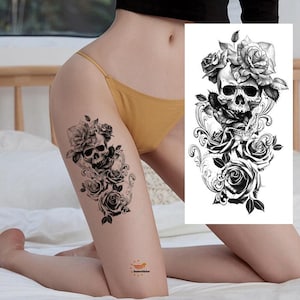 Könnte beinhalten: Schwarz-weiß temporäres Tattoo mit einem Totenkopf-Design mit Rosen. Das Tattoo ist auf dem Oberschenkel angebracht und zeigt die komplizierten floralen und Totenkopf-Kunstwerke. Das Design umfasst detaillierte Schattierungen und florale Elemente.