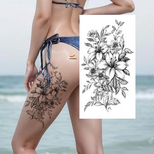 May include: Black and white floral temporary tattoo featuring lilies and other flowers. The tattoo is applied to the thigh, with a matching design on a white background.