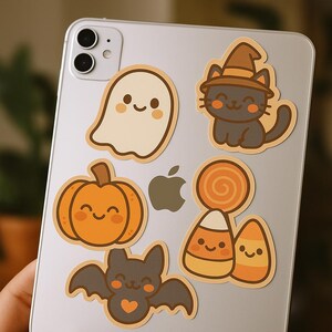 Könnte beinhalten: Eine Sammlung von Halloween-Stickern mit einem lächelnden Geist, einer schwarzen Katze mit Hexenhut, einem Kürbis, einer Fledermaus und Zuckermais. Die Aufkleber sind in Orange-, Braun- und Beigetönen gehalten.