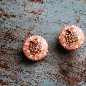 May include: Two pink round knobs with white polka dots and a red and white plaid apple design.