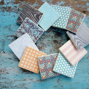 May include: A set of ten square coasters with various patterns, including floral, geometric, and wood grain designs. The coasters are arranged in a circle on a blue wooden surface.