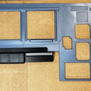 Peut inclure: Maquette en plastique bleu-gris d'un tableau de bord de véhicule, avec diverses découpes rectangulaires et carrées. Le modèle comprend une section ressemblant au côté conducteur avec une fenêtre et un haut-parleur, et une zone de console centrale.