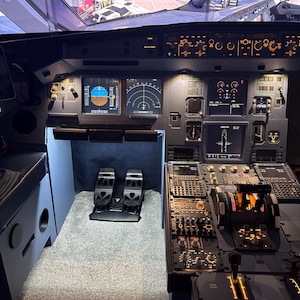 May include: An aircraft cockpit interior, showcasing a complex array of digital displays and control panels. The image highlights the flight instruments, levers, and foot pedals. The cockpit is illuminated, emphasizing the various controls and displays.