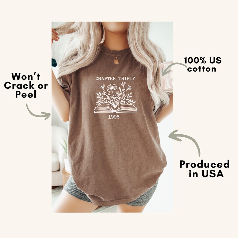 May include: A brown short-sleeve t-shirt featuring a white graphic of an open book with flowers emerging from the pages. The text reads CHAPTER THIRTY and 1996. Additional text on the image states Won't Crack or Peel, 100% US cotton, and Produced in USA.