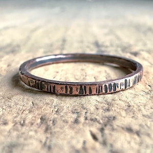May include: A thin copper band ring with a hammered texture. The ring has a dark brown patina and a smooth, polished interior.