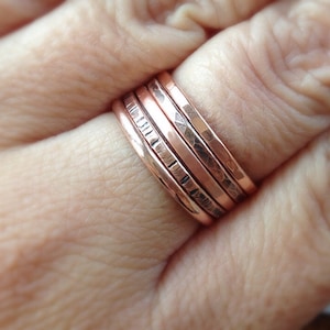 May include: A set of five thin copper rings stacked on a finger. The rings are hammered and have a slightly textured finish.