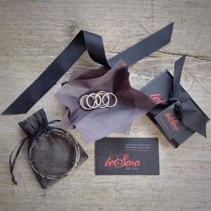 May include: A set of silver rings in a black box with a black and white logo that reads "te Soro Del Sol" and the text "HANDCRAFTED EXOTIC BOHEMIAN JEWELLERY BY SANDY BAGLIANO".
