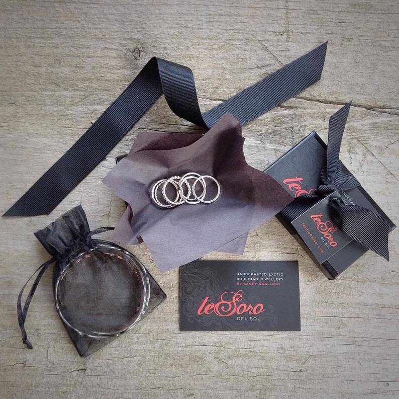 May include: A set of silver rings in a black box with a black and white logo that reads "te Soro Del Sol" and the text "HANDCRAFTED EXOTIC BOHEMIAN JEWELLERY BY SANDY BAGLIANO".