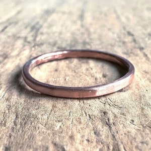 May include: A simple, thin, rose gold band ring. The ring is smooth and has a slightly hammered finish.