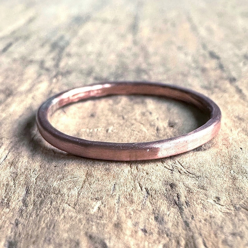 May include: A simple, thin, rose gold band ring. The ring is smooth and has a slightly hammered finish.