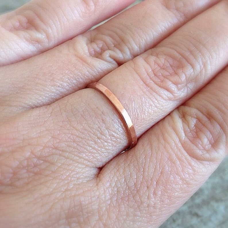 May include: A thin, rose gold band ring worn on a finger.