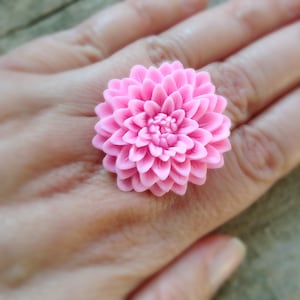 以下が含まれることがあります： 詳細な花びらのピンクの花の指輪。 このリングは、鮮やかなピンクの色合いの大きな3次元ダリアデザインが特徴です。 このフローラルリングは、どんな服装にも自然にインスパイアされたフレアを加えるのに最適な、ステートメントピースです。