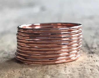 Op de afbeelding: Een stapel van tien gehamerde koperen ringen. Elke ring is dun en heeft een getextureerd oppervlak. De ringen zijn op elkaar gestapeld, waardoor een gelaagd effect ontstaat. Het koper heeft een warme, roodbruine kleur.