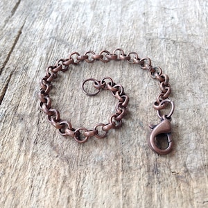 Op de afbeelding: Een koperen kettingarmband met een karabijn sluiting. De ketting is gemaakt van kleine, ronde schakels.
