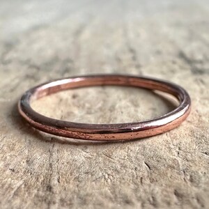 May include: A simple, thin, rose gold band ring.