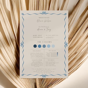 Op de afbeelding: Een trouwuitnodigingskaart met een lichtbeige achtergrond en een blauwe decoratieve rand. De tekst bevat de namen van de bruid en bruidegom, de datum, de locatie en het kleurenpalet. De kaart is versierd met een blauw lintontwerp.