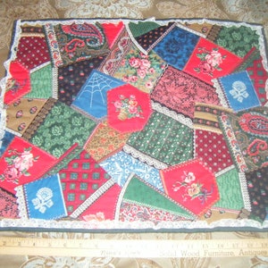 May include: A colorful patchwork quilt with a variety of patterns and fabrics, including floral, paisley, and geometric designs. The quilt is edged with white lace and has a dark green border.