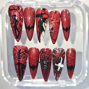 May include: A set of ten stiletto-shaped press-on nails featuring a vibrant red glitter base. The designs include black silhouettes of figures, bat motifs, detailed anime-style character portraits, a 3D rose, and intricate white and black accents.